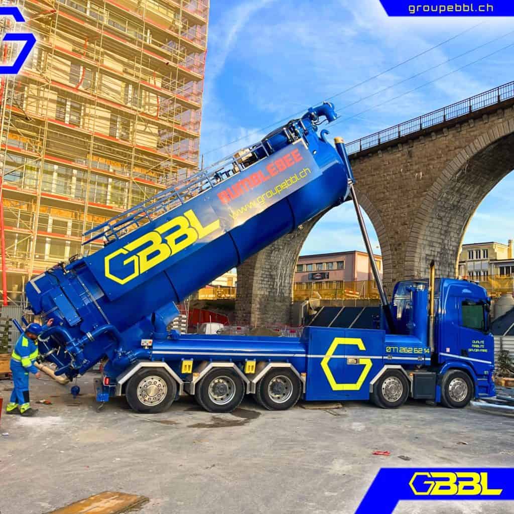 Camion de pompage de béton bleu avec logo GBBL, chantier en arrière-plan.