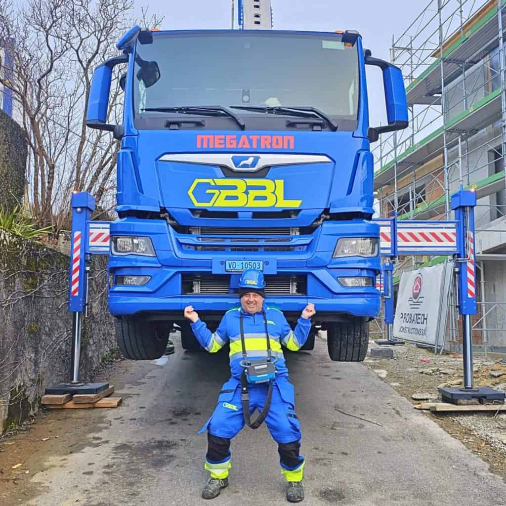 Camion de levage bleu avec un opérateur devant, chantier en arrière-plan.
