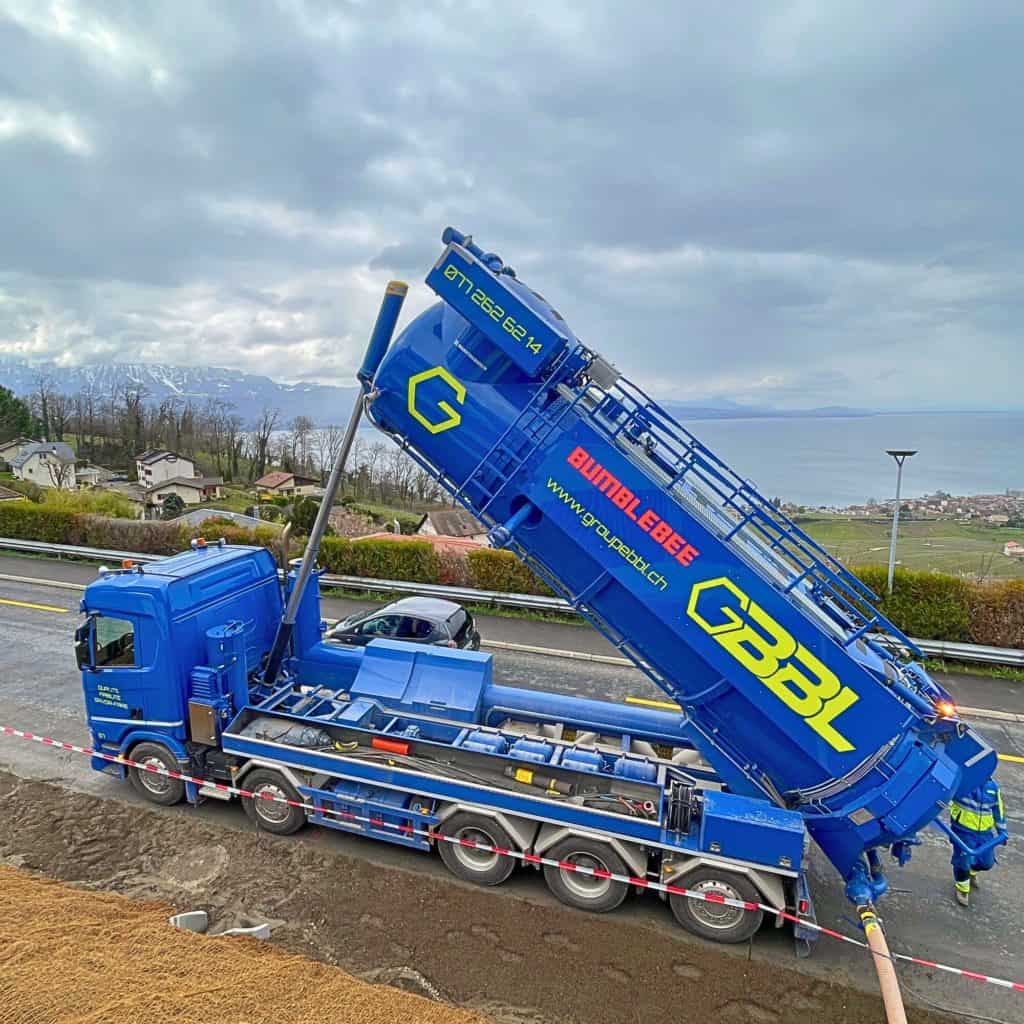 Camion de construction bleu avec bras mécanique en position inclinée.