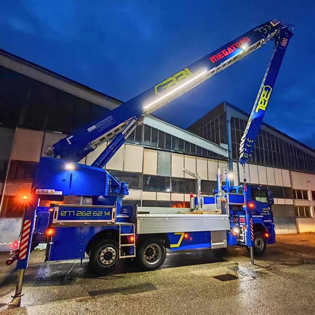 Camion-grue bleu pour levage lourd devant un bâtiment moderne la nuit.