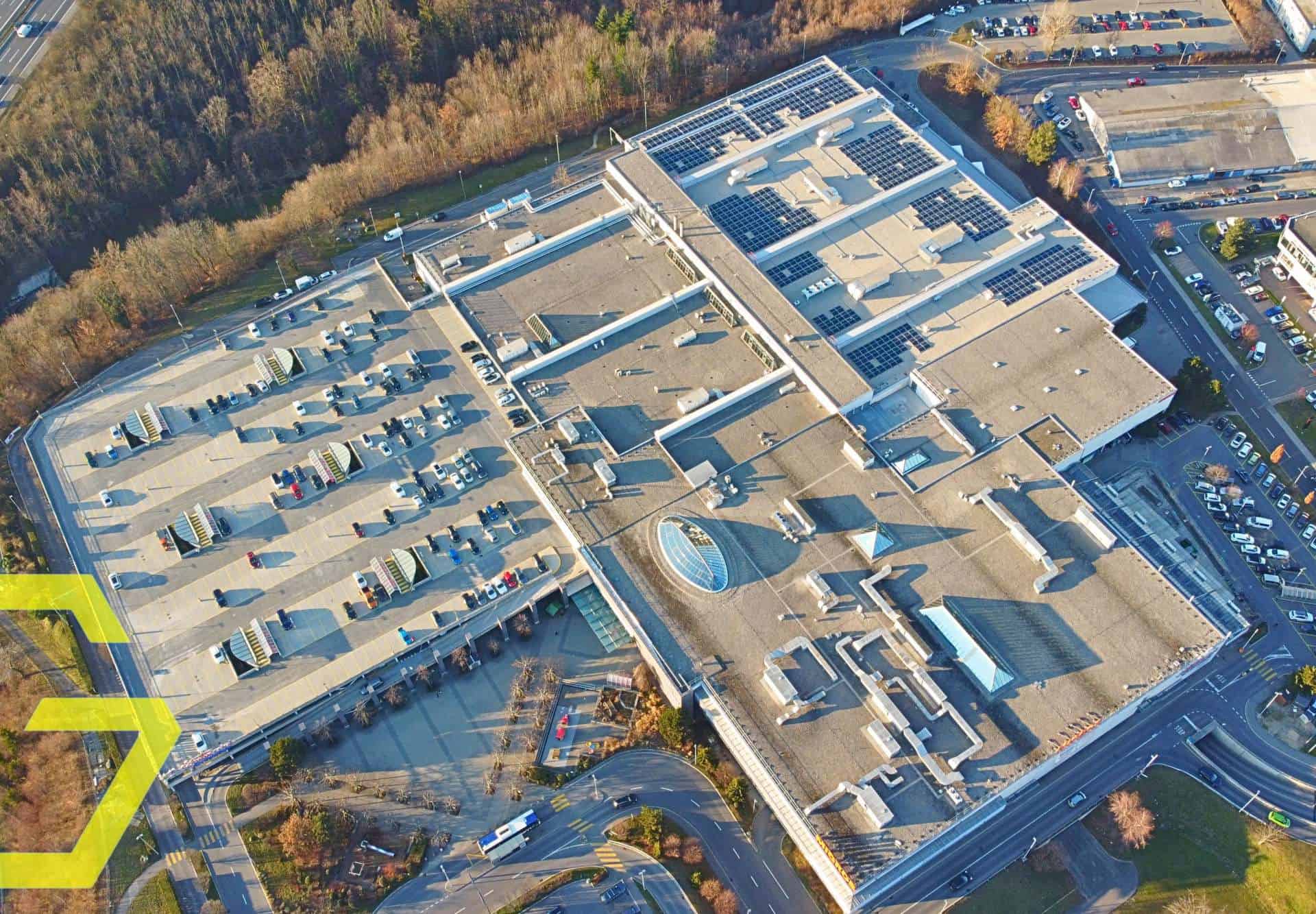 Vue aérienne du centre commercial BBL SA à Crissier avec parking et toitures solaires.