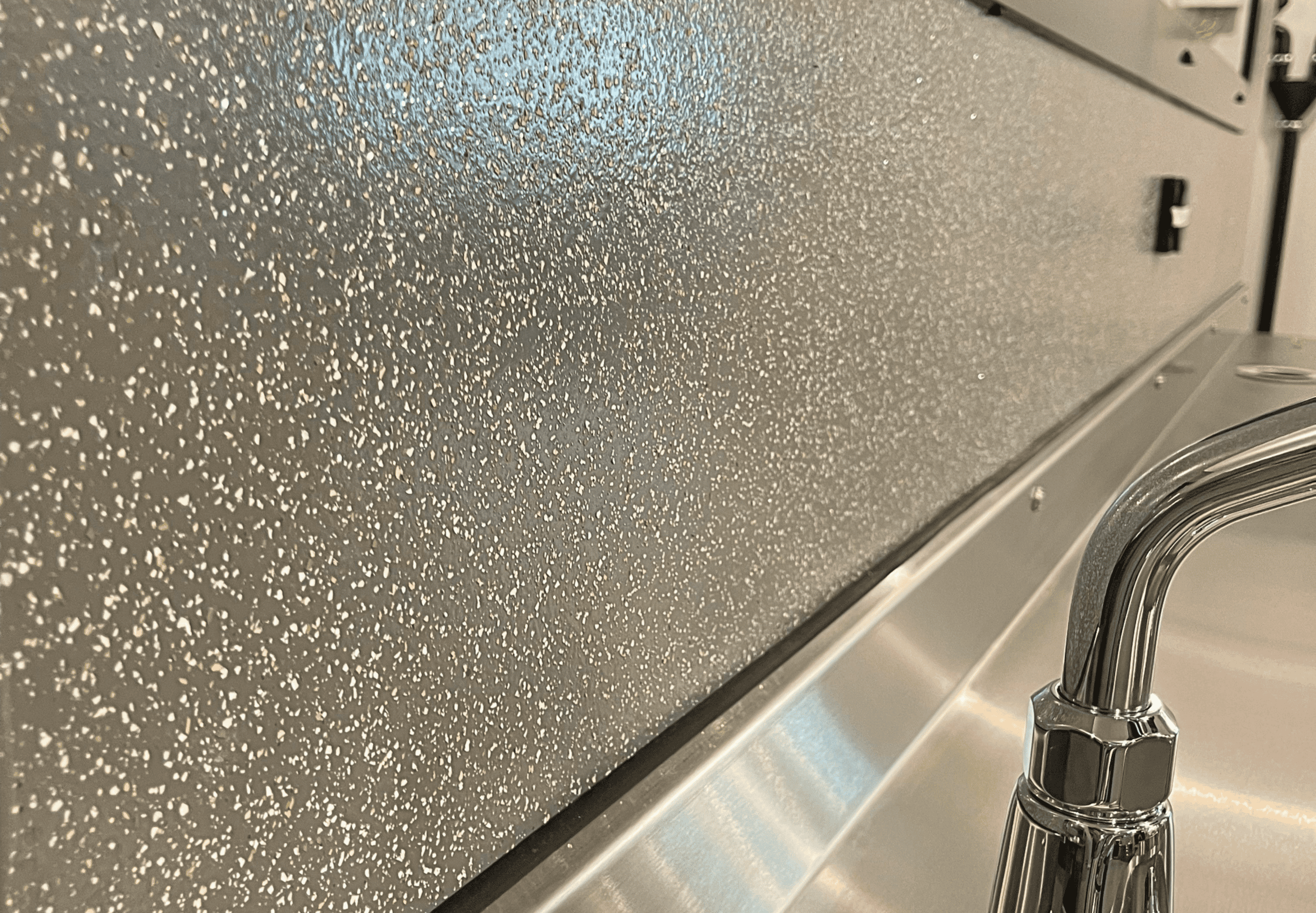 Surface en acier inoxydable avec texture granuleuse, près d'un robinet en métal.