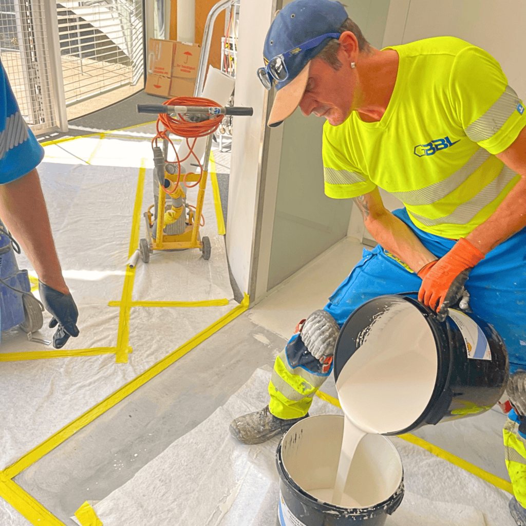Travailleur en chantier appliquant de la peinture ou du plâtre, portant équipement de sécurité.